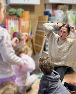 Creative arts therapist Amber Jackson sitting on the floor with preschool children, using expressive body movements during a group session at Koru Allied Therapies.