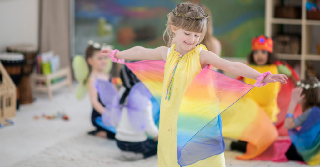 A young girl in a yellow dress dancing with rainbow silk scarves during a creative arts therapy session for children in the Illawarra