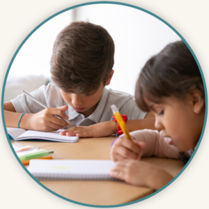 Two children sitting at a table writing in notebooks, representing the focused handwriting practice in Koru Allied Therapies' Handwriting Helpers program