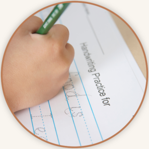 Close-up of a child's hand holding a green pencil, tracing dotted letters on lined handwriting practice paper