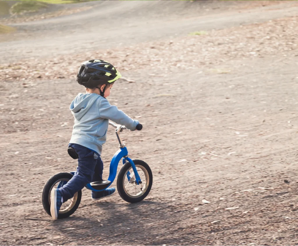 A young child riding a balance bike along a dirt track, building balance and confidence