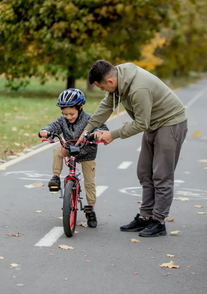 An adult supporting a child learning to ride a two-wheel bike on a bike path